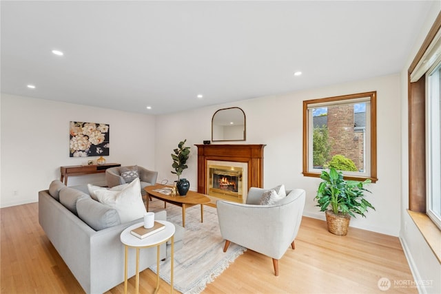 living area featuring light wood finished floors, recessed lighting, a glass covered fireplace, and baseboards