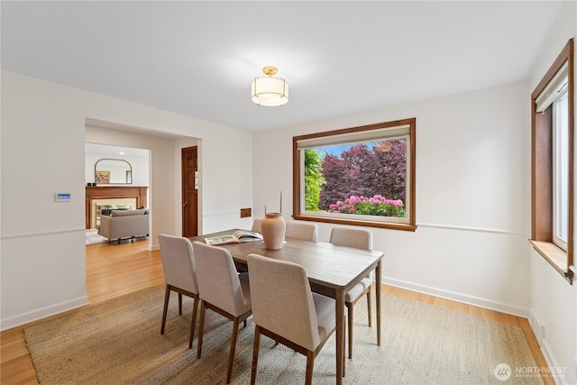 dining area with light wood-style floors, a fireplace, and baseboards