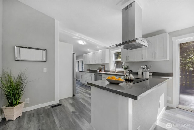 kitchen with dishwasher, island exhaust hood, dark countertops, white cabinets, and light wood-type flooring