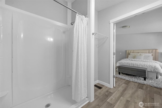 bathroom featuring a stall shower, baseboards, ensuite bath, and wood finished floors