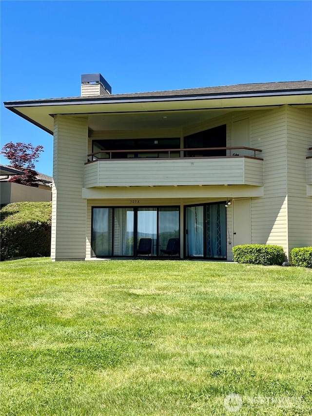 back of house featuring a yard, a chimney, and a balcony