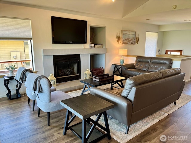 living area featuring a tiled fireplace, wood finished floors, and baseboards