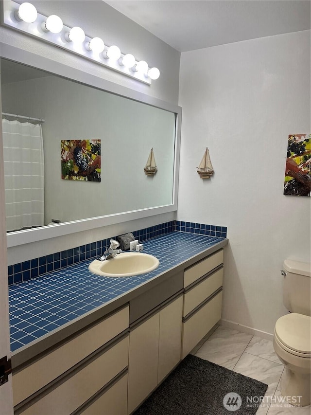 bathroom featuring toilet, marble finish floor, baseboards, and vanity