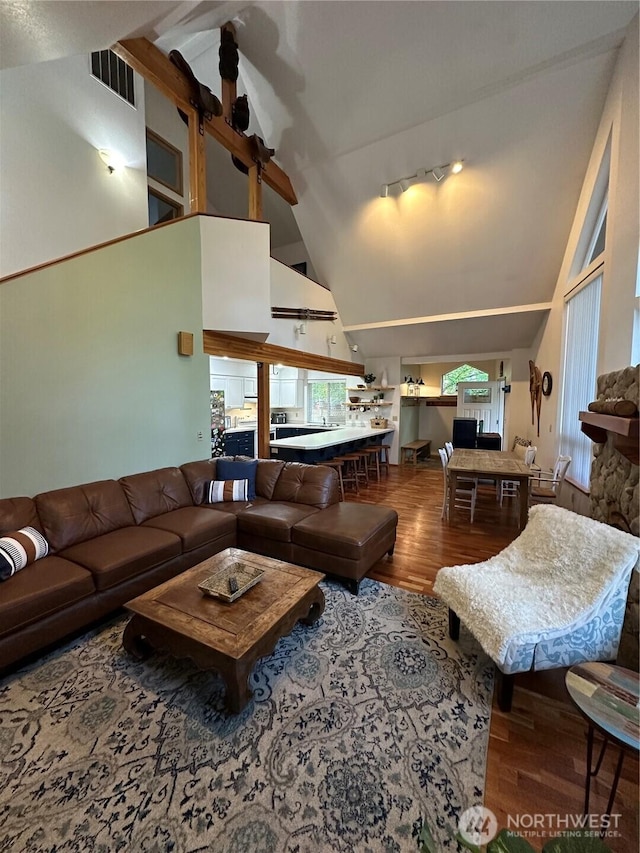 living area with wood finished floors, high vaulted ceiling, track lighting, and beam ceiling