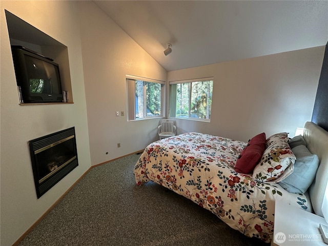 carpeted bedroom featuring lofted ceiling, baseboards, and a glass covered fireplace