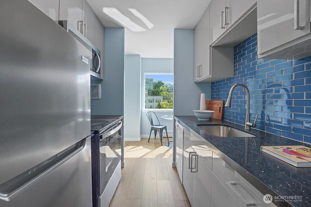 kitchen with stainless steel appliances, a sink, light wood-type flooring, tasteful backsplash, and dark stone countertops