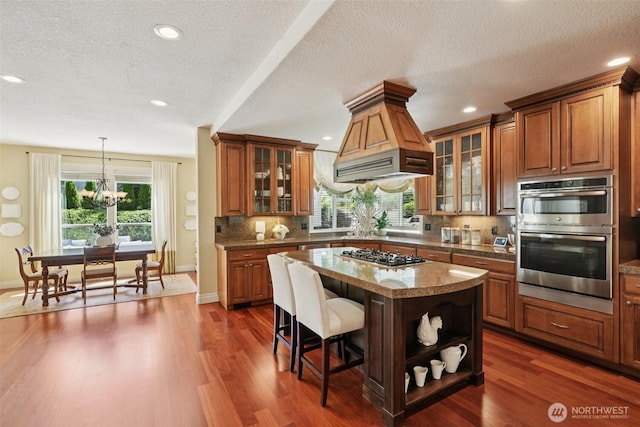 1610 NW 34th Ave, Camas, WA 98607 - kitchen featuring appliances with stainless steel finishes, custom range hood, brown cabinets, a kitchen breakfast bar, and backsplash