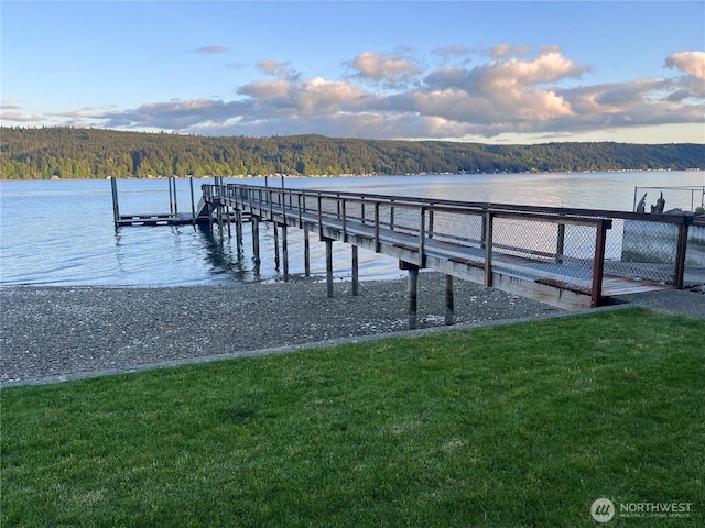 dock area with a wooded view, a yard, and a water view