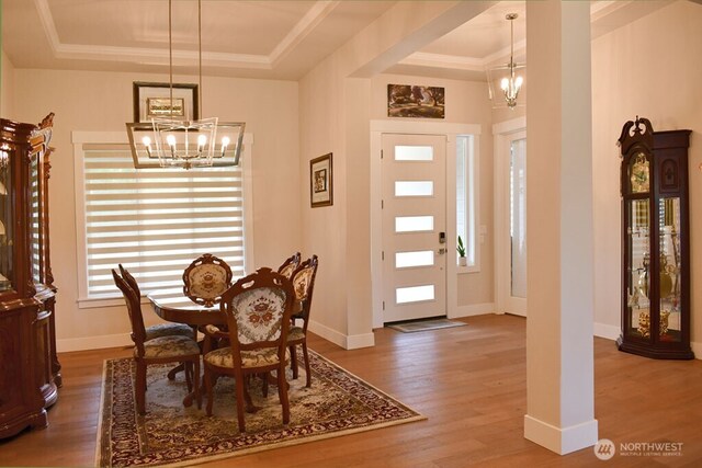 dining area featuring a chandelier, a raised ceiling, wood finished floors, baseboards, and crown molding