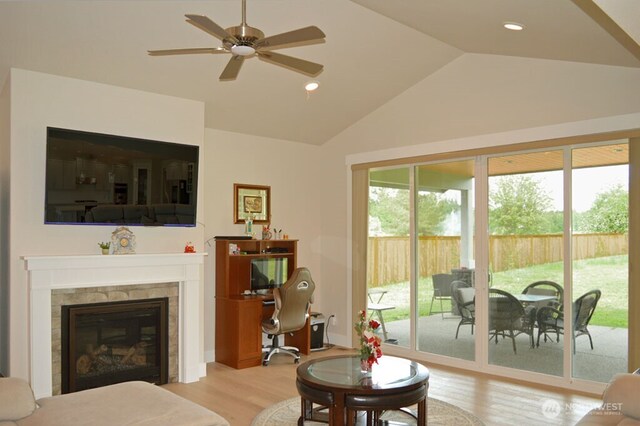living area with wood finished floors, lofted ceiling, a desk, a tiled fireplace, and ceiling fan