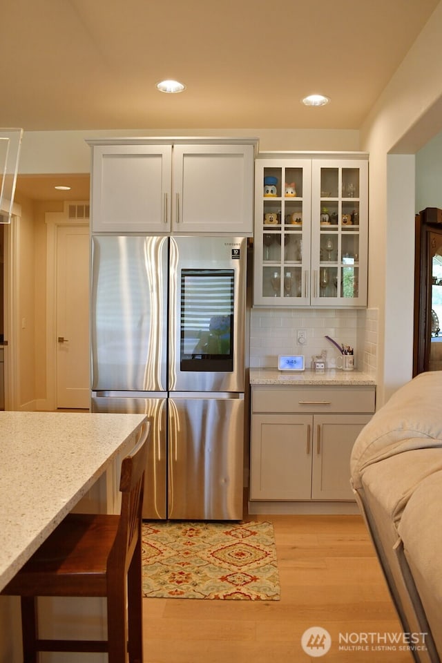 kitchen with smart refrigerator, light wood-type flooring, tasteful backsplash, glass insert cabinets, and light stone countertops