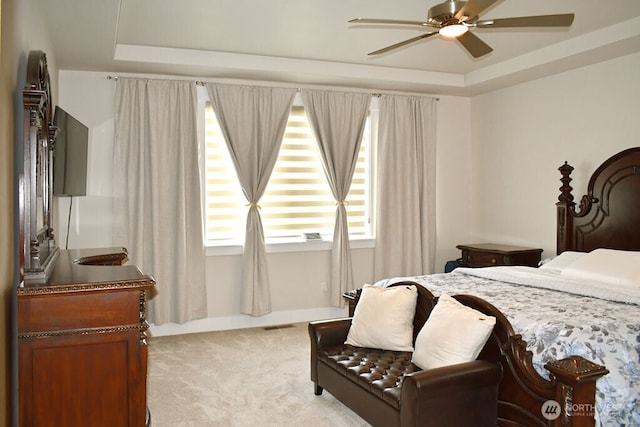 bedroom featuring light colored carpet, a tray ceiling, and ceiling fan