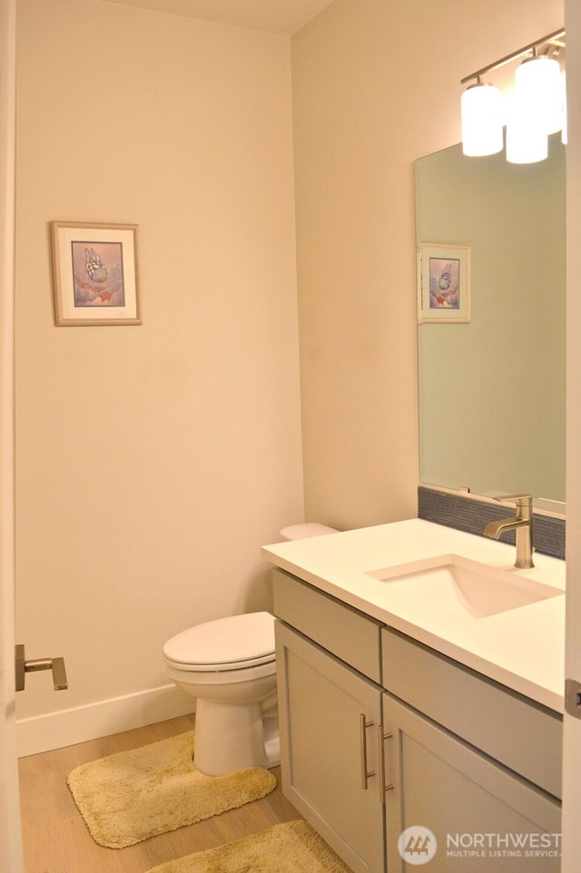 bathroom with toilet, vanity, baseboards, and wood finished floors