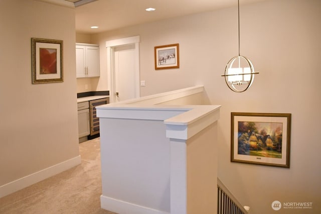 corridor featuring beverage cooler, light colored carpet, baseboards, recessed lighting, and a chandelier
