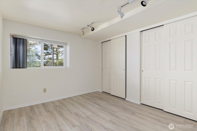 4966 Bradley Ln, Freeland, WA 98249 - unfurnished bedroom featuring a closet, rail lighting, baseboards, and light wood-type flooring