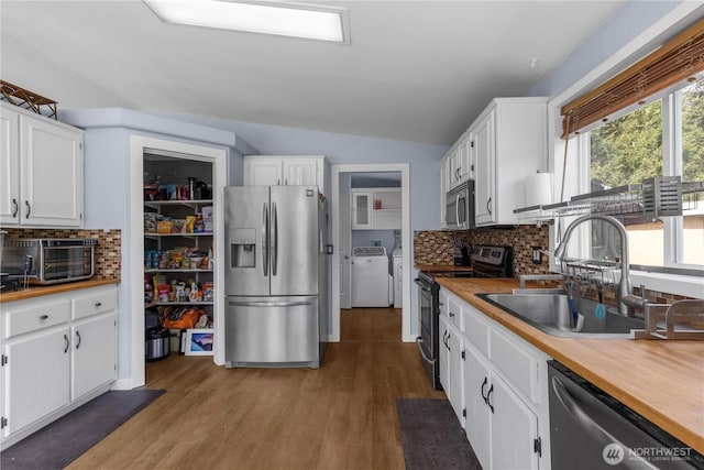 kitchen with appliances with stainless steel finishes, washer and dryer, a sink, white cabinets, and lofted ceiling