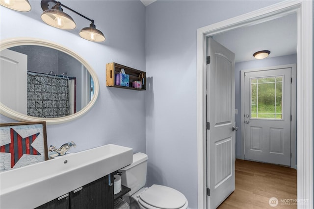 bathroom featuring wood finished floors, toilet, curtained shower, and a sink