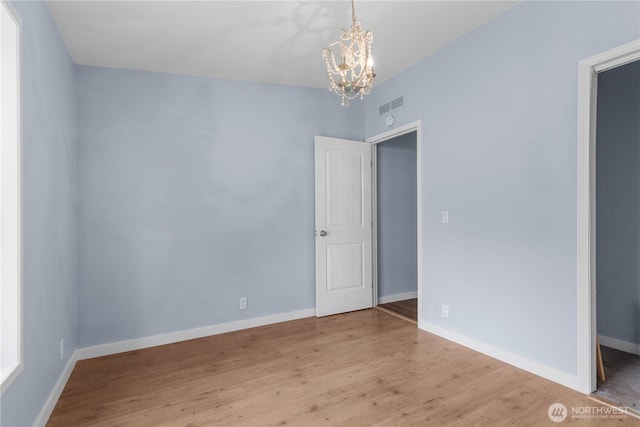unfurnished room with a chandelier, wood finished floors, and baseboards