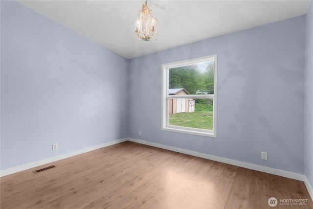 empty room with baseboards, a chandelier, and wood finished floors