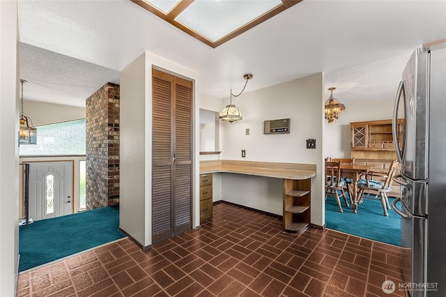 kitchen with freestanding refrigerator, decorative light fixtures, brick patterned floor, and baseboards