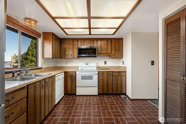 kitchen featuring brown cabinets, a sink, light countertops, brick floor, and white appliances