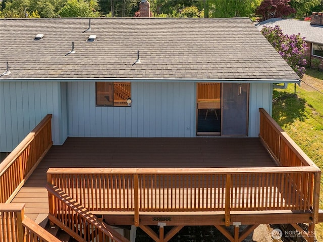 exterior space with roof with shingles, a wooden deck, and a chimney
