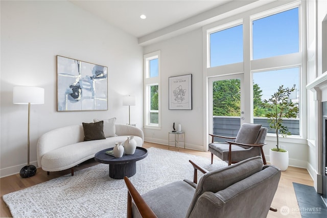 living area with light wood-type flooring, baseboards, a high ceiling, recessed lighting, and a fireplace with flush hearth