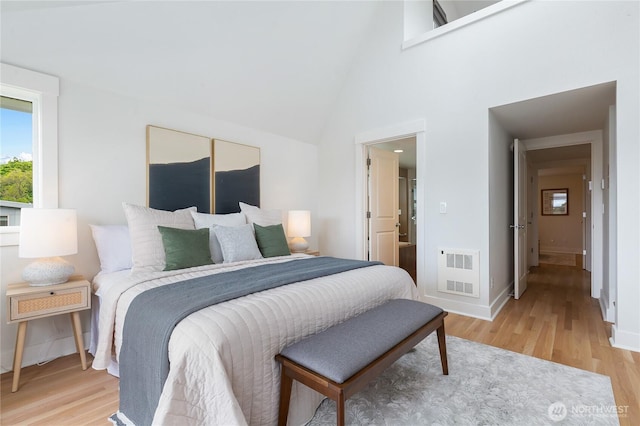 bedroom featuring light wood-type flooring, baseboards, and high vaulted ceiling