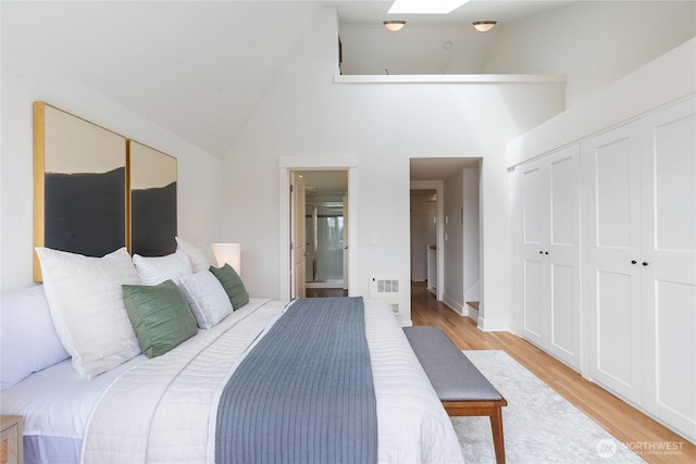 bedroom featuring light wood-style floors, high vaulted ceiling, a closet, ensuite bath, and a skylight