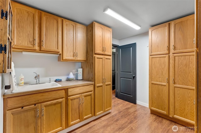 kitchen with a sink, light wood-style floors, light countertops, and baseboards