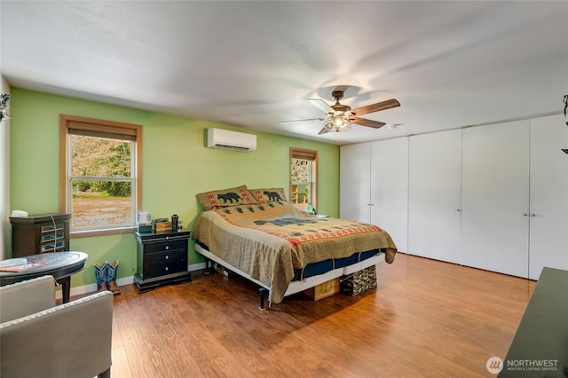 bedroom with a wall unit AC, wood finished floors, and a ceiling fan