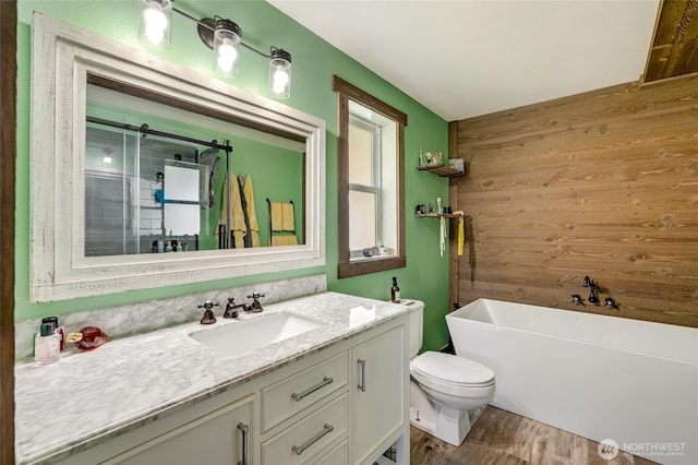 bathroom featuring vanity, wooden walls, a freestanding tub, wood finished floors, and toilet