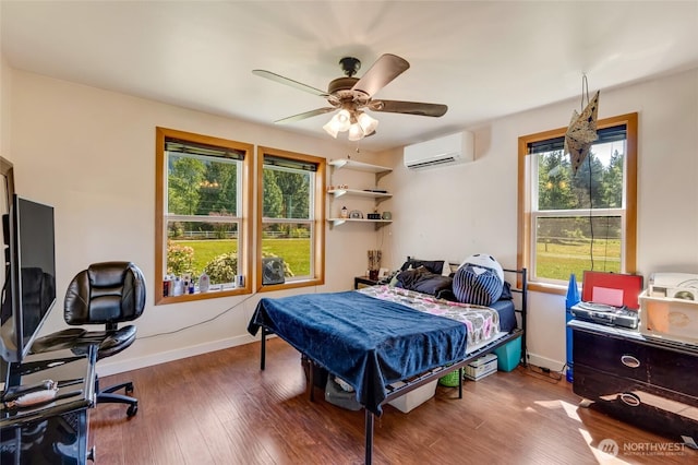 bedroom featuring a wall unit AC, a desk, wood finished floors, baseboards, and ceiling fan