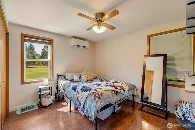 bedroom with a wall unit AC, wood finished floors, baseboards, and ceiling fan