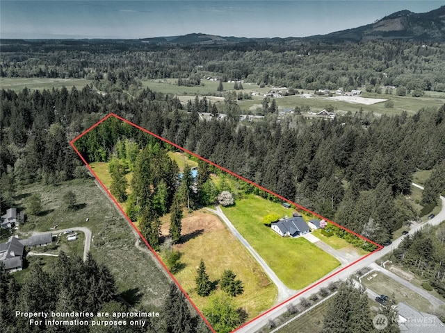 aerial view of property and surrounding area with a forest, property parcel outlined, and a mountain backdrop