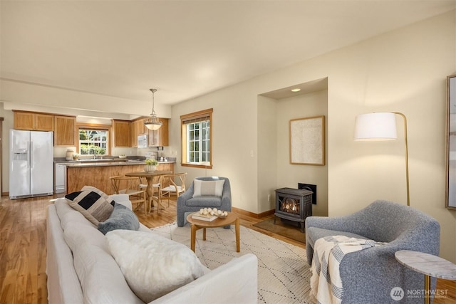 living area featuring a wood stove, baseboards, and light wood finished floors
