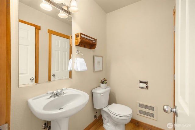 half bath with heating unit, toilet, baseboards, a sink, and wood finished floors
