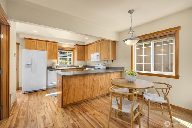 kitchen with a peninsula, a sink, dark countertops, light wood-type flooring, and white appliances
