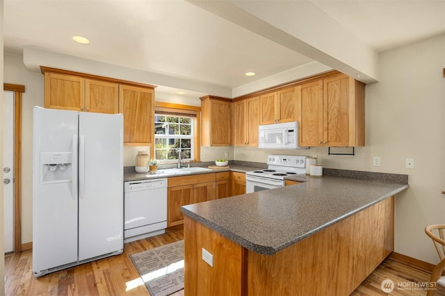 kitchen with light wood finished floors, dark countertops, a sink, and white appliances