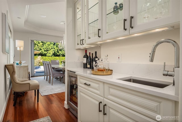 indoor dry bar featuring dark wood-type flooring, a tray ceiling, wine cooler, and ornamental molding