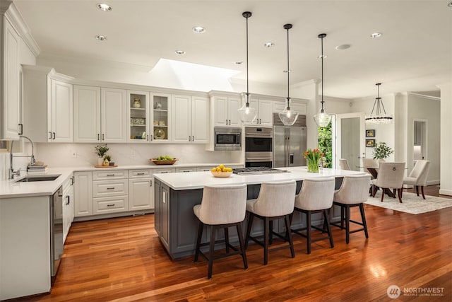 kitchen with built in appliances, a sink, crown molding, a kitchen island, and a breakfast bar