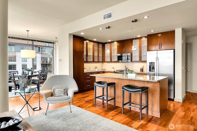 2121 Terry Ave Unit N1203, Seattle, WA 98121 - kitchen featuring stainless steel appliances, light wood-style flooring, glass insert cabinets, a kitchen island with sink, and a breakfast bar area