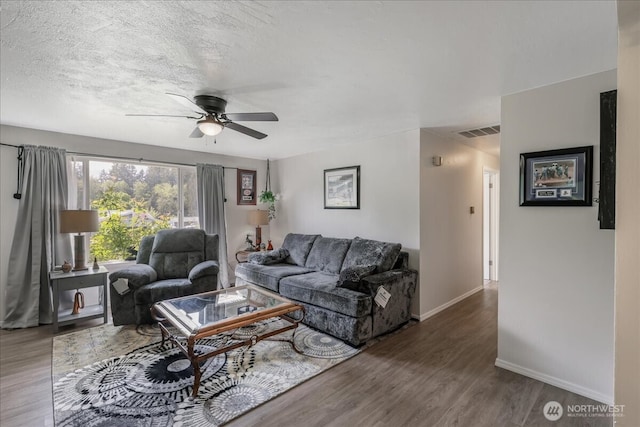 living room with a textured ceiling, baseboards, ceiling fan, visible vents, and wood finished floors