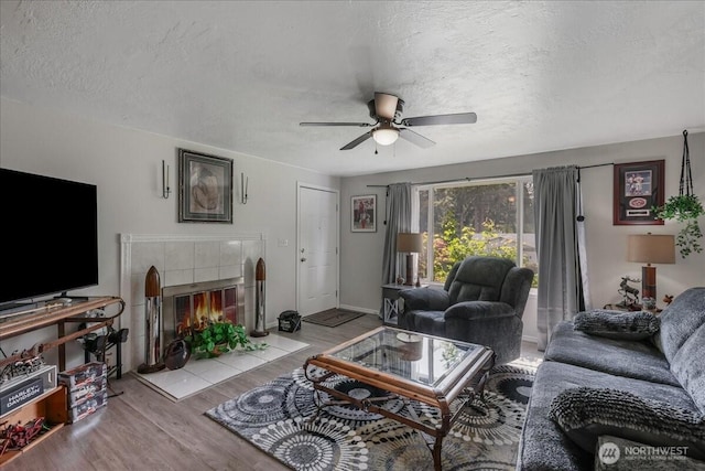 living room with a textured ceiling, wood finished floors, baseboards, and ceiling fan
