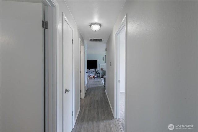 corridor with light wood-style flooring, baseboards, and visible vents