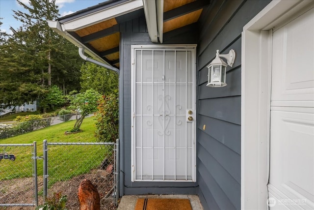 view of exterior entry featuring a lawn and fence