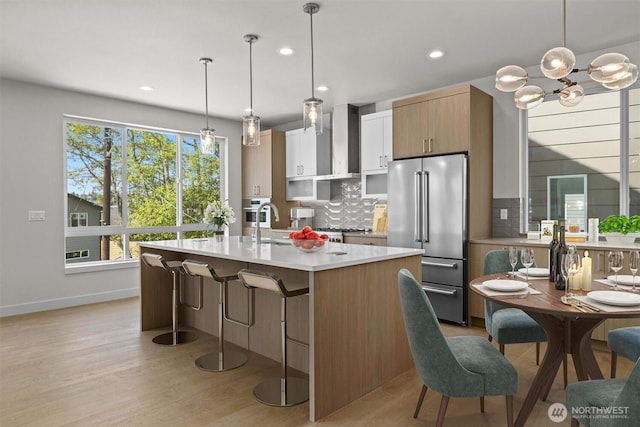 kitchen with wall chimney exhaust hood, decorative backsplash, light countertops, high end refrigerator, and baseboards