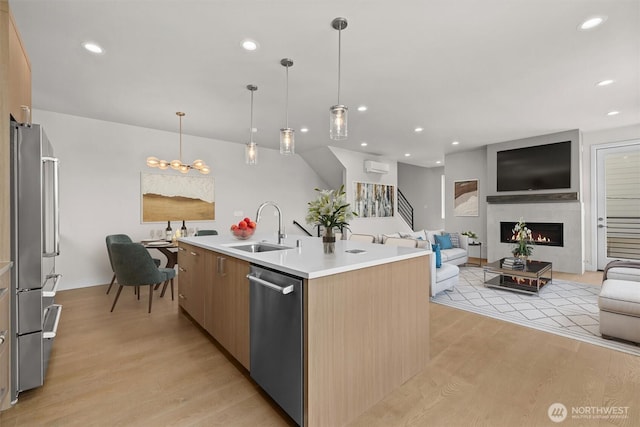 kitchen with a sink, light wood-style flooring, open floor plan, and appliances with stainless steel finishes