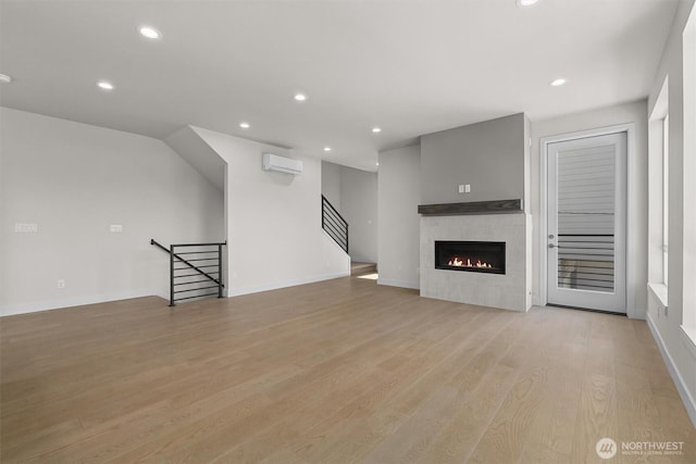 unfurnished living room featuring a wall mounted air conditioner, recessed lighting, baseboards, a glass covered fireplace, and light wood-type flooring