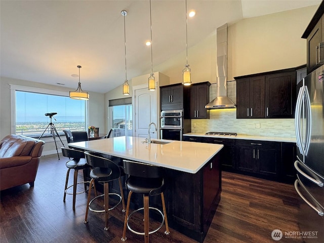 kitchen featuring a sink, stainless steel appliances, wall chimney range hood, backsplash, and dark wood-style floors